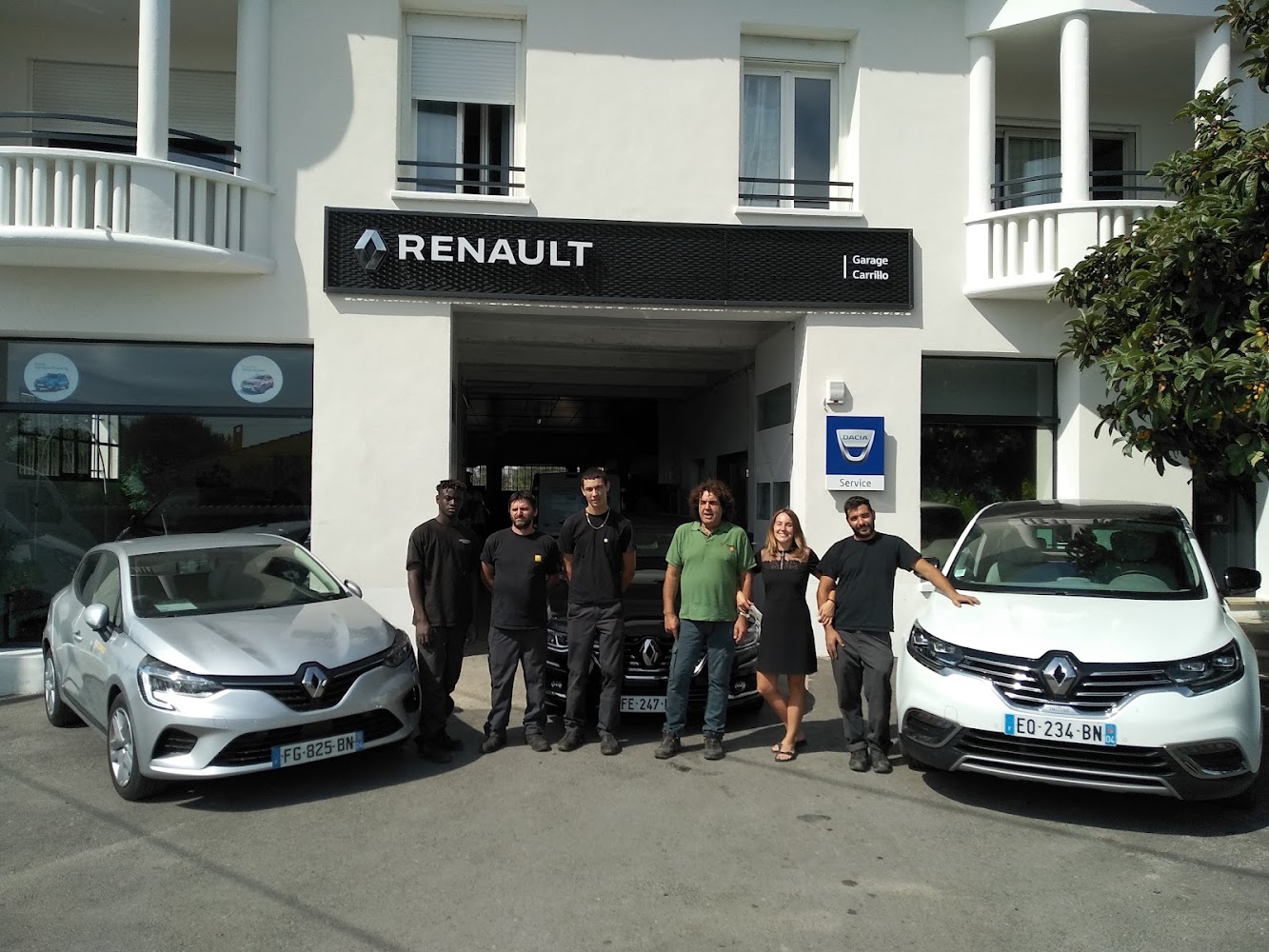 L'équipe du Garage Carrillo posant devant la façade Renault de l'atelier, entre une Clio grise et un Espace blanc